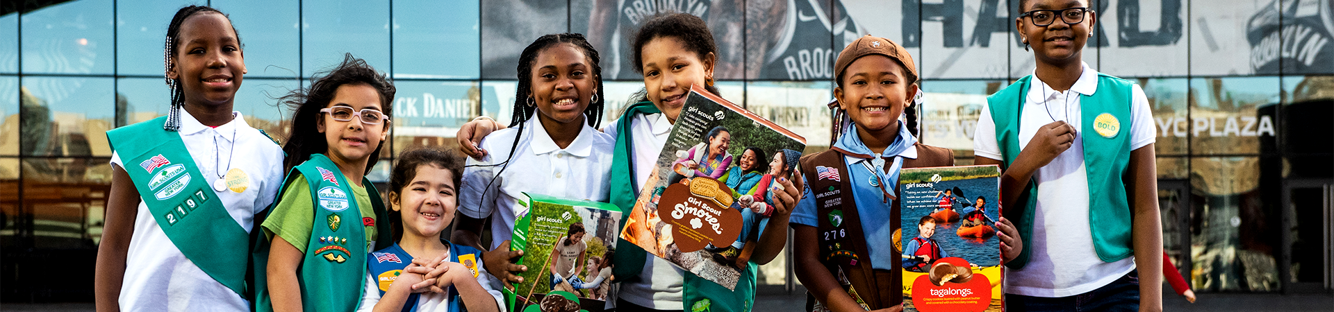  girl scouts selling cookies with one girl in front of booth holding sign that says "girl scout cookie proceeds stay local" 