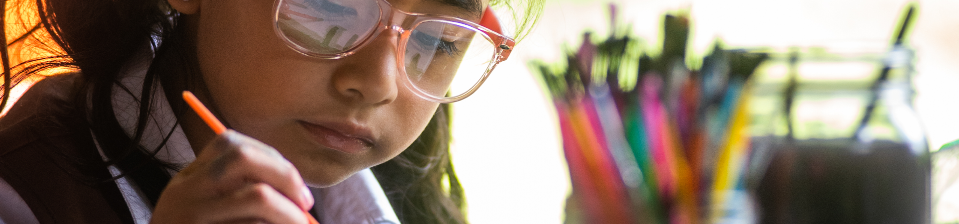  A Girl Scout drawing a picture with a jar of many colored pencils next to her. 