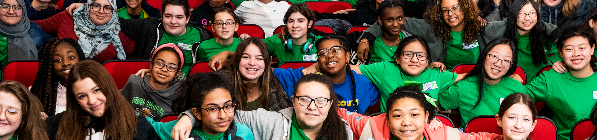  Girl Scouts sitting in an auditorium with their arms around each other, wearing matching Leadership Institute t-shirts. 