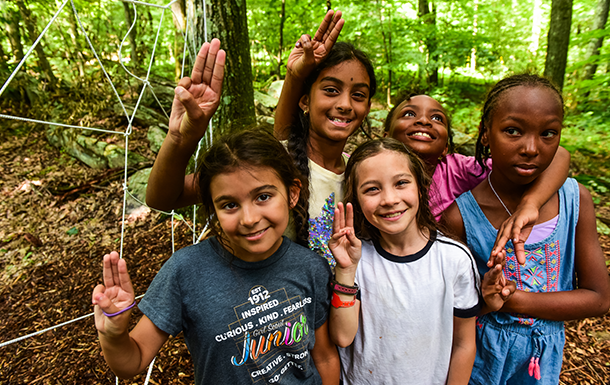 group of daisy girl scouts holding hands in uniform blue apron vest with patches and badges