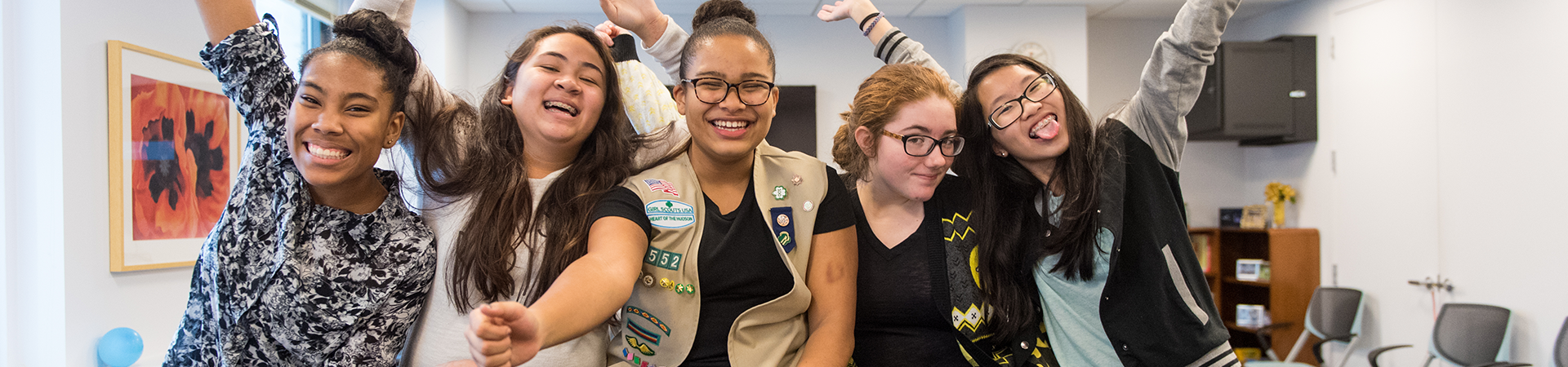  group of junior girl scouts walking outside hugging smiling at camera in junior vest and sash with badges 