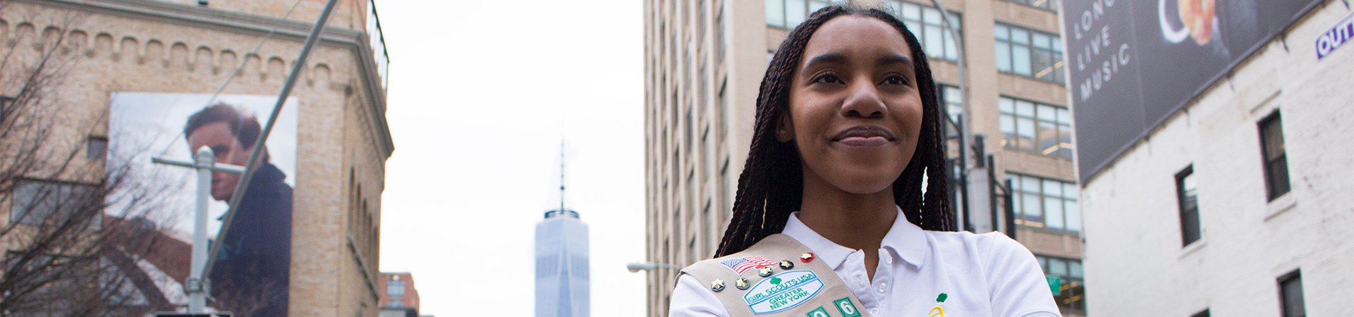  High school girl in Girl Scout sash and winter jacket smiling at camera against green backdrop. 