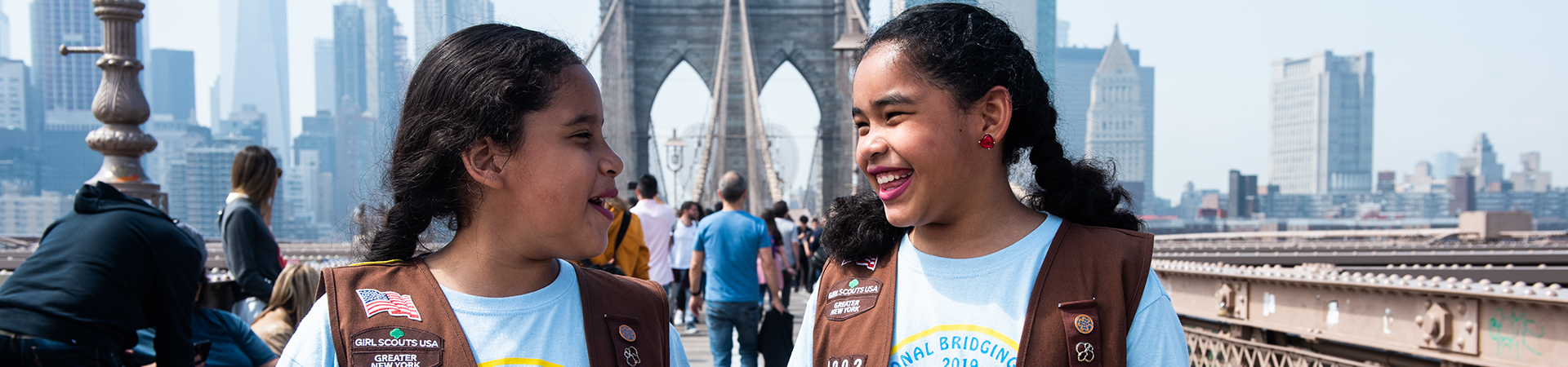  two girl scouts wearing trefoil clothing leaning on one another indoors 