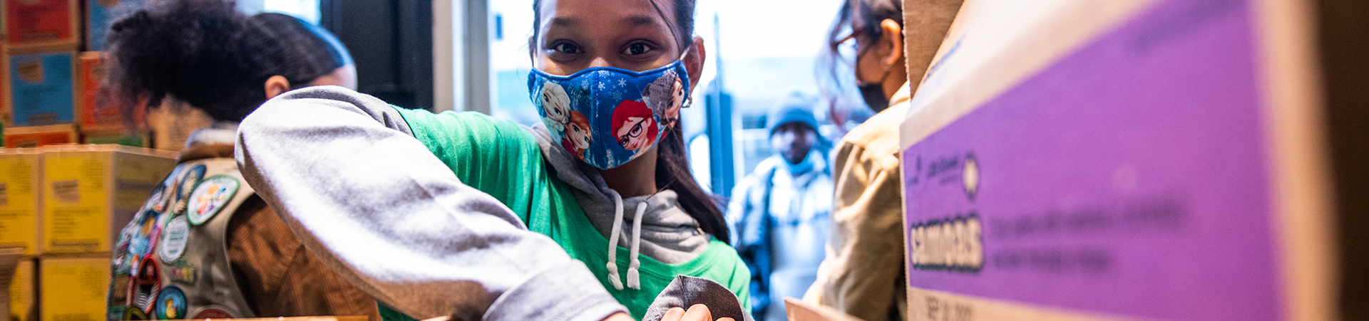  Girl Socut at a cookie sale wearing a mask, reaching for cookies 