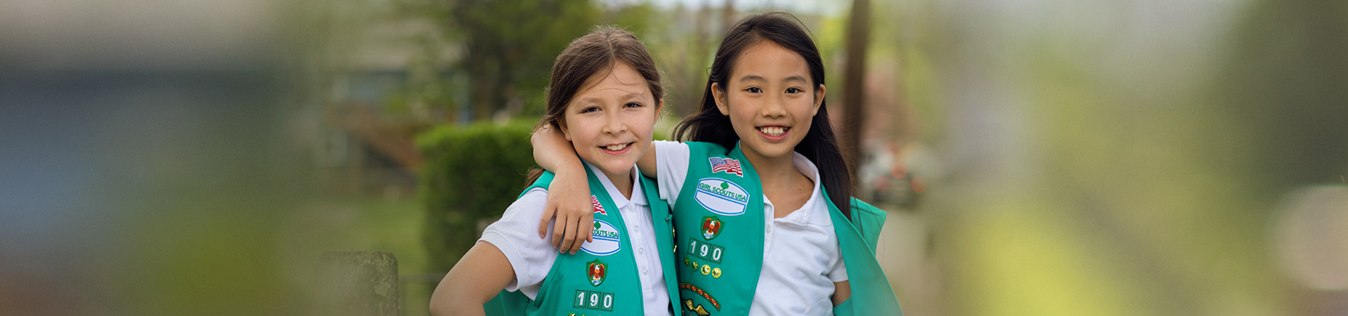  two girl scout juniors outside wearing junior vest uniform smiling and hugging 